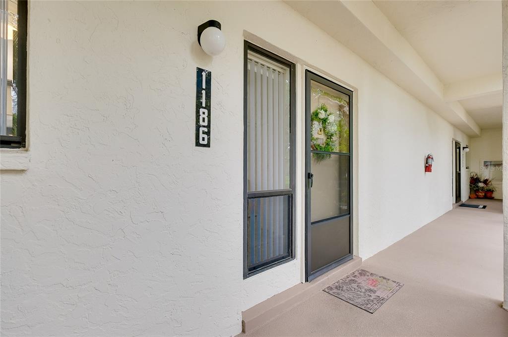 A white exterior wall features a vertical address plaque, a light fixture, and a door — 1186 BIRD BAY WAY UNIT 109, VENICE, FL