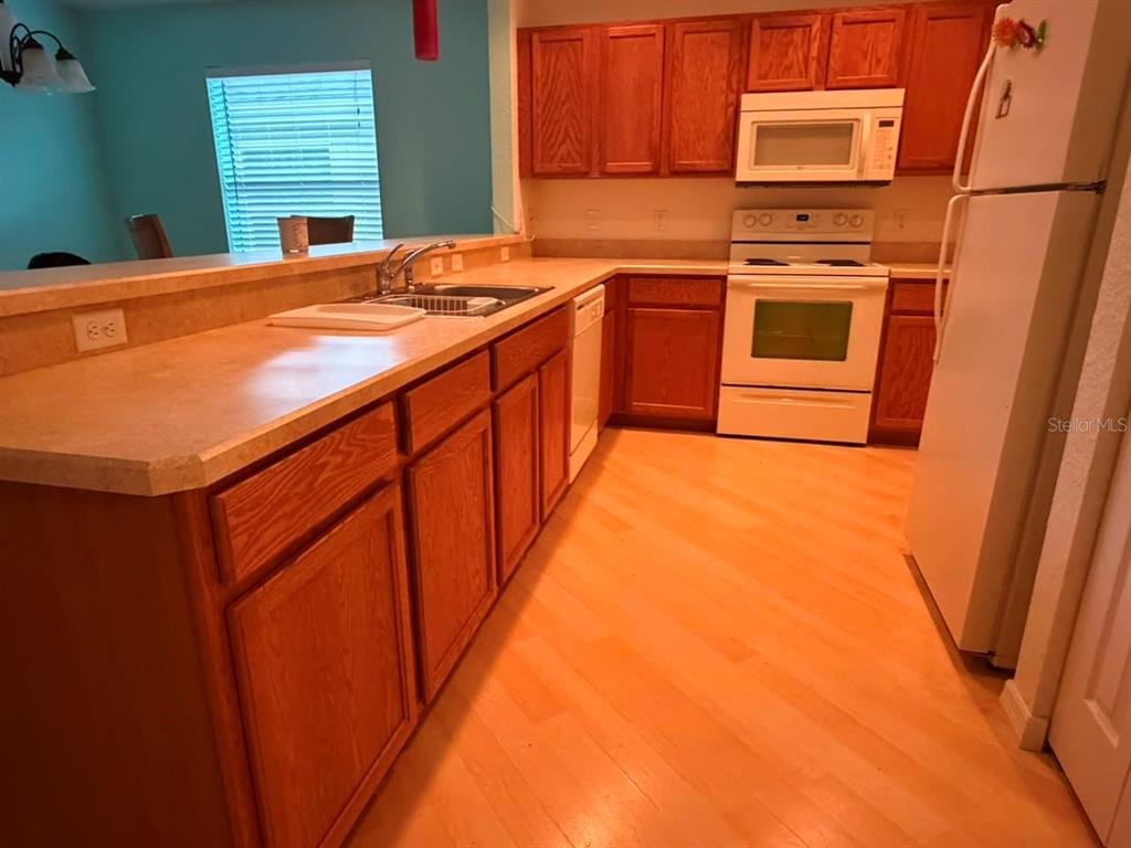 A kitchen features wood cabinets, white appliances, and a laminate countertop with a breakfast bar — 4921 NE 123RD LANE, OXFORD, FL