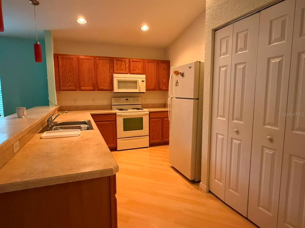 A kitchen features wood cabinets, white appliances, laminate countertops, and light-colored wood flooring — 4921 NE 123RD LANE, OXFORD, FL