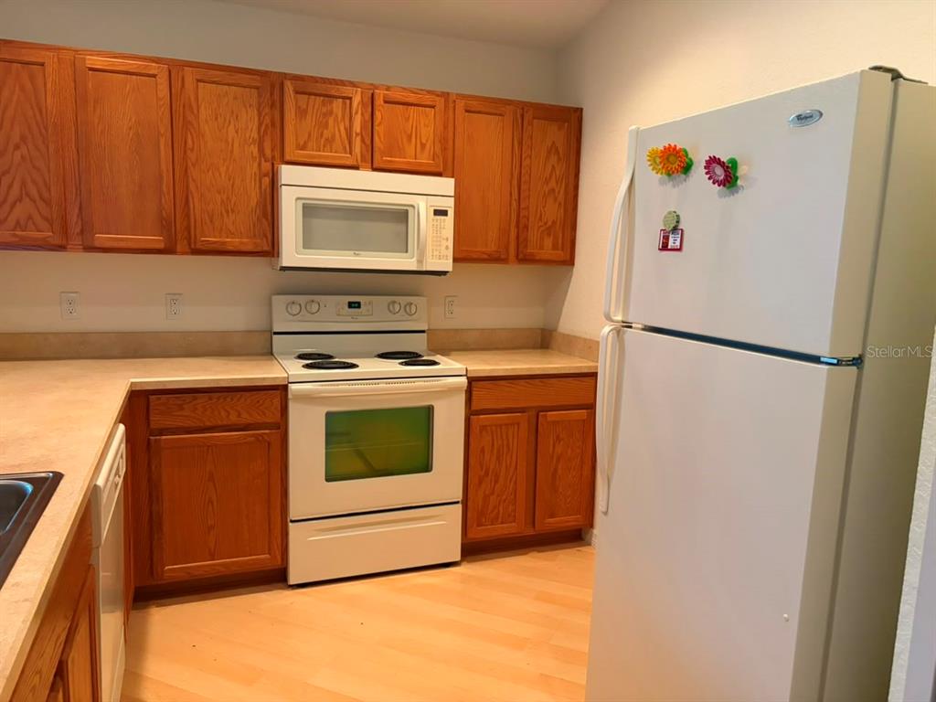 A kitchen features wood cabinets, white appliances, and light-colored countertops — 4921 NE 123RD LANE, OXFORD, FL