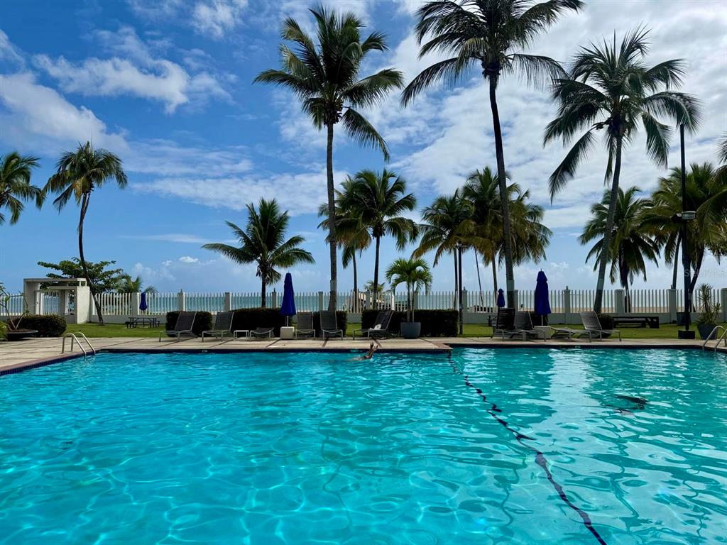A swimming pool overlooks a beach with palm trees and a white fence — 187 HORIZONTE UNIT 906, CAROLINA, PR