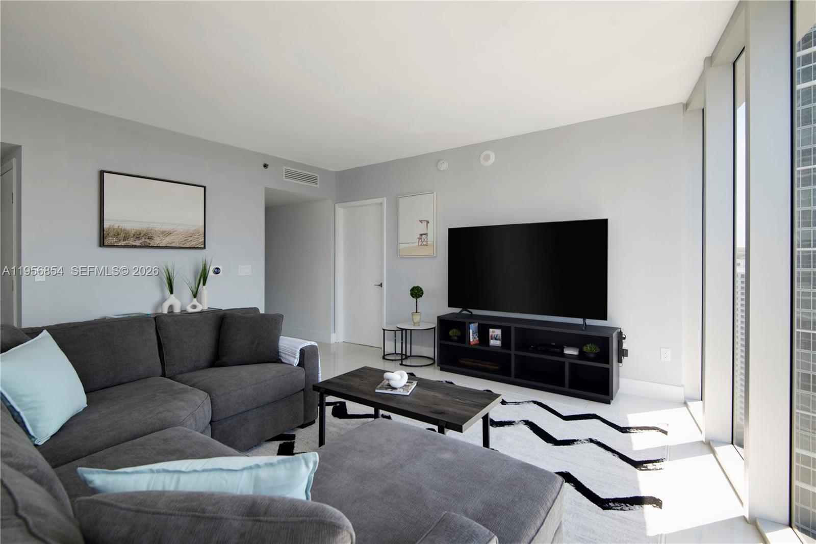 A living room features a grey sectional sofa, a television on a stand, and a rug — 485 Brickell Ave # 3208, Miami FL 33131, MIAMI, FL