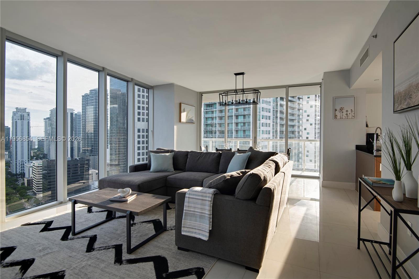 A modern living room features a gray sectional sofa, a coffee table, and floor-to-ceiling windows — 485 Brickell Ave # 3208, Miami FL 33131, MIAMI, FL