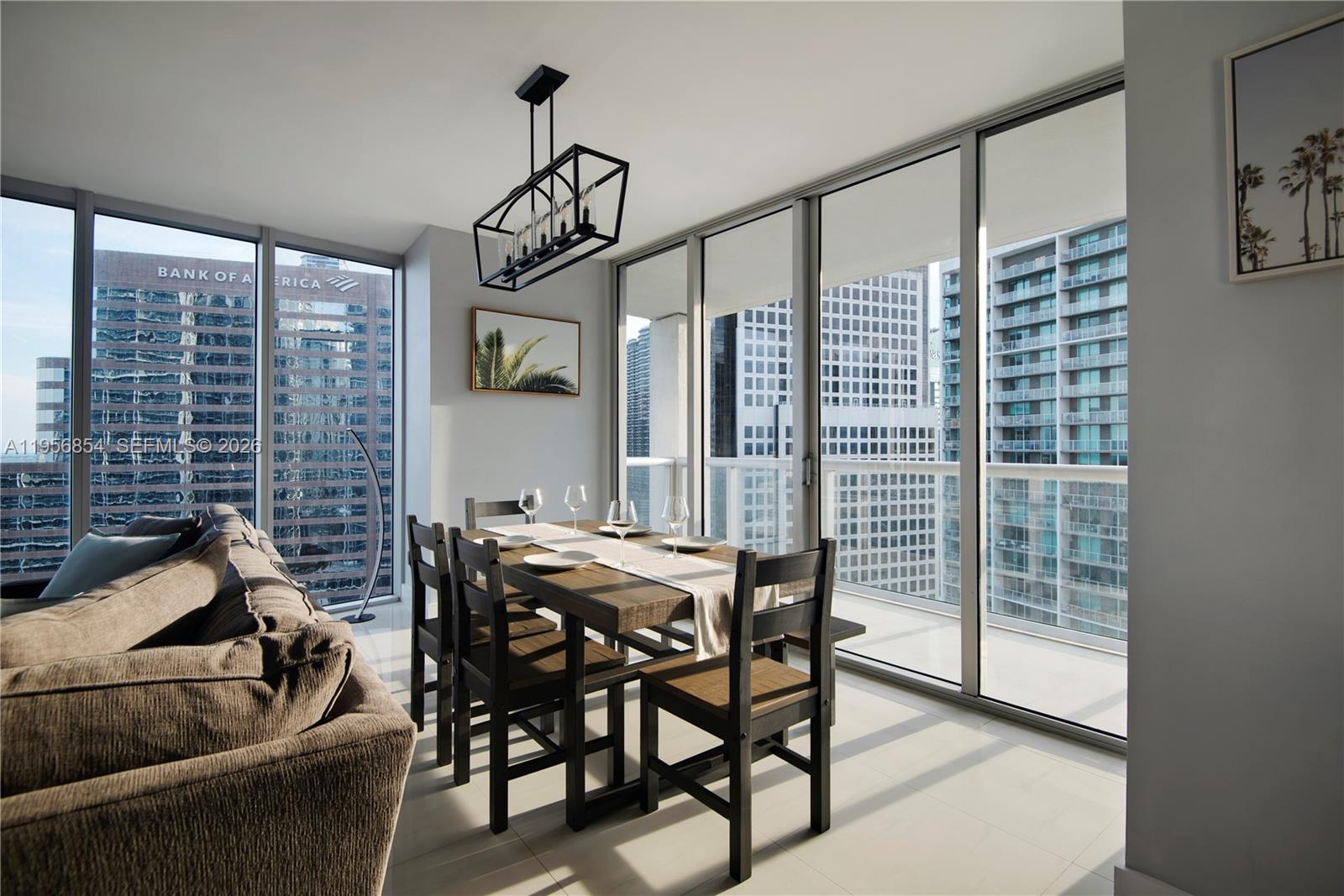 A dining area with a wooden table and chairs sits beside floor-to-ceiling windows overlooking city buildings — 485 Brickell Ave # 3208, Miami FL 33131, MIAMI, FL