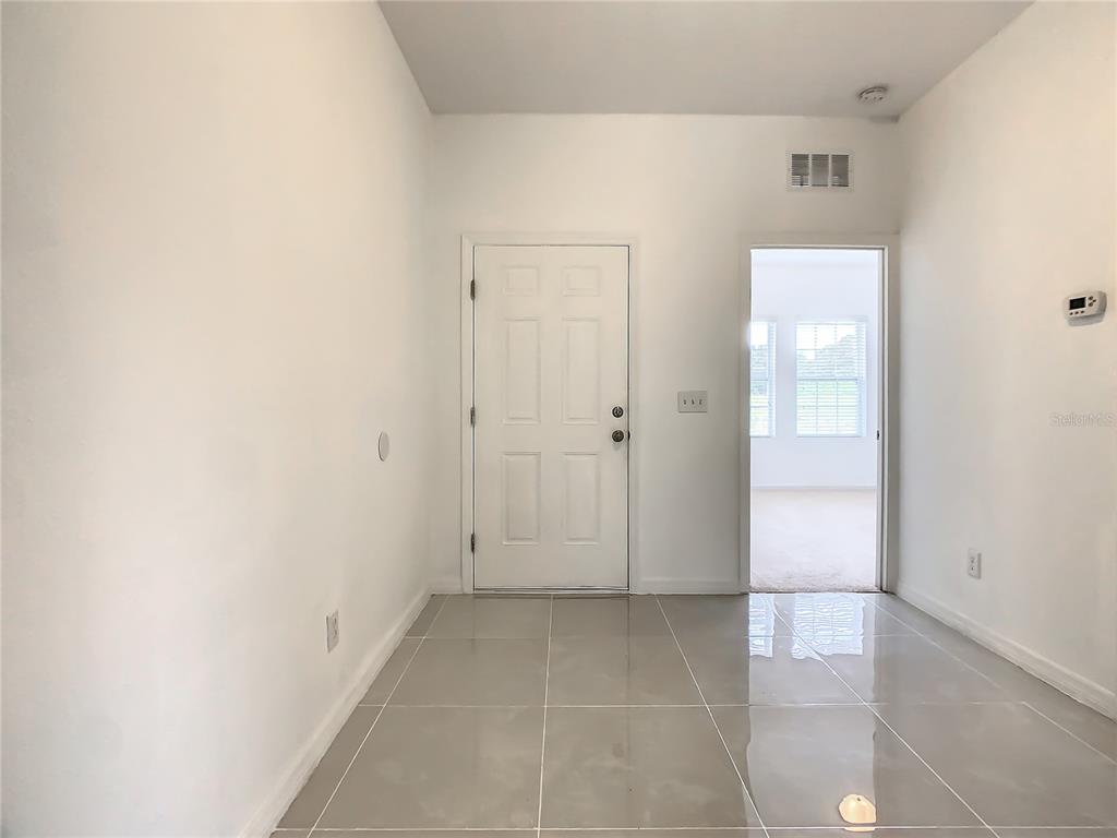 An entryway with light-colored tile flooring, a white front door, and a doorway to another room — 1025 MARGOT LANE, LAKE WALES, FL