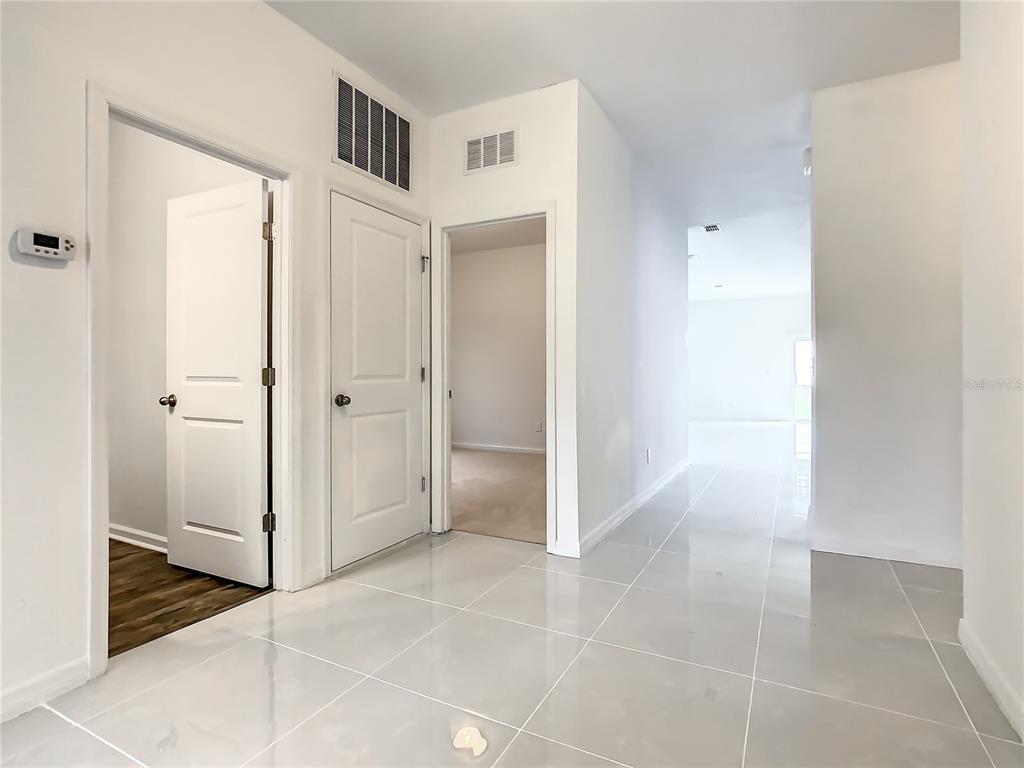 A hallway with light-colored tile flooring leads to a room with carpeted floors — 1025 MARGOT LANE, LAKE WALES, FL