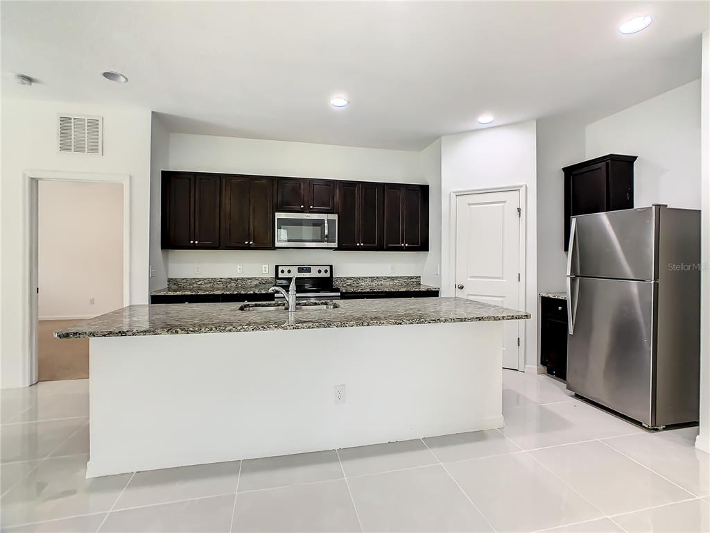 A kitchen features dark wood cabinets, granite countertops, a center island, and stainless steel appliances — 1025 MARGOT LANE, LAKE WALES, FL