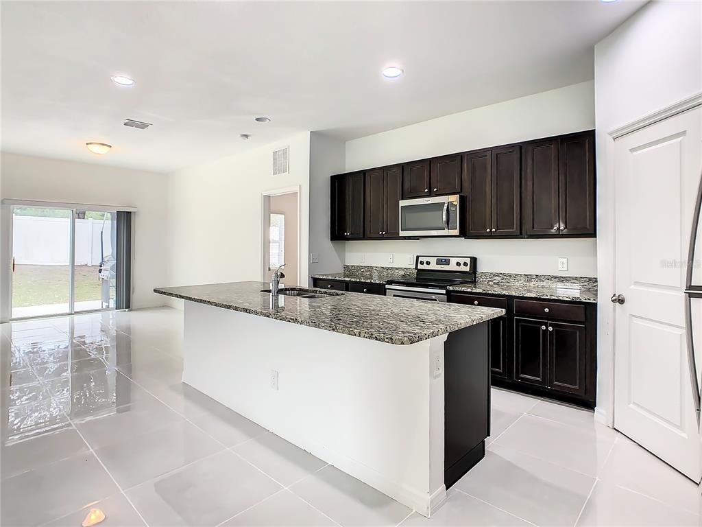 A kitchen features dark wood cabinets, granite countertops, a center island, and light tile flooring — 1025 MARGOT LANE, LAKE WALES, FL