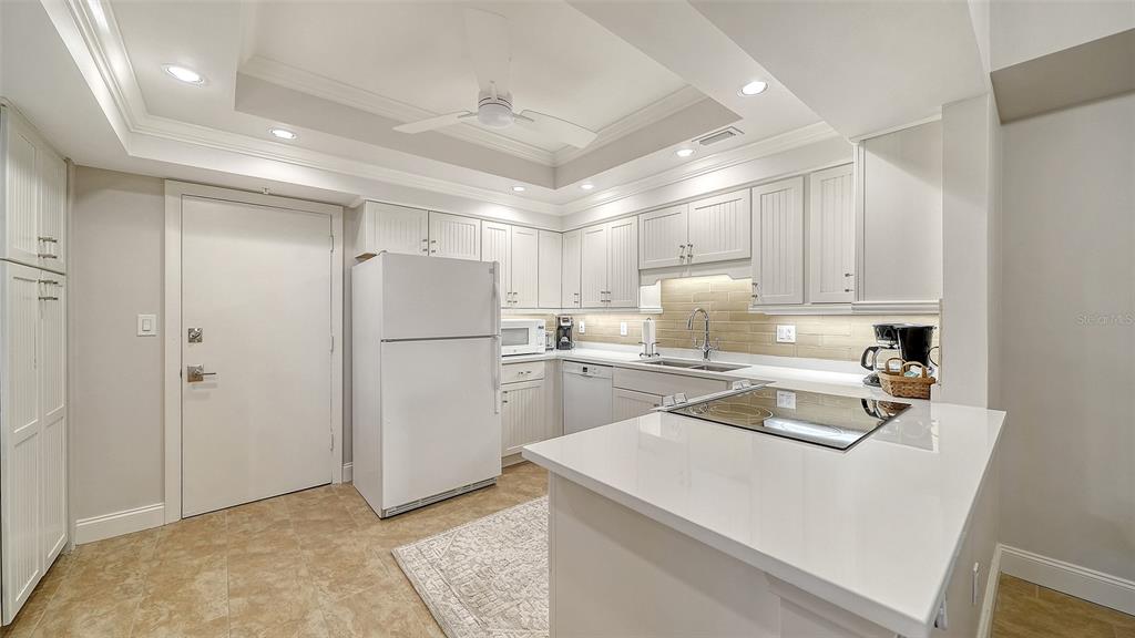 A kitchen features white cabinets, a white refrigerator, a quartz countertop, and a tile backsplash — 2301 GULF OF MEXICO DRIVE UNIT 11N, LONGBOAT KEY, FL