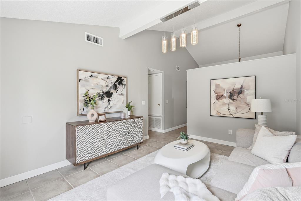 A living room features a vaulted ceiling, tiled floors, a patterned sideboard, and a sectional sofa — 16206 SAGEBRUSH ROAD, TAMPA, FL