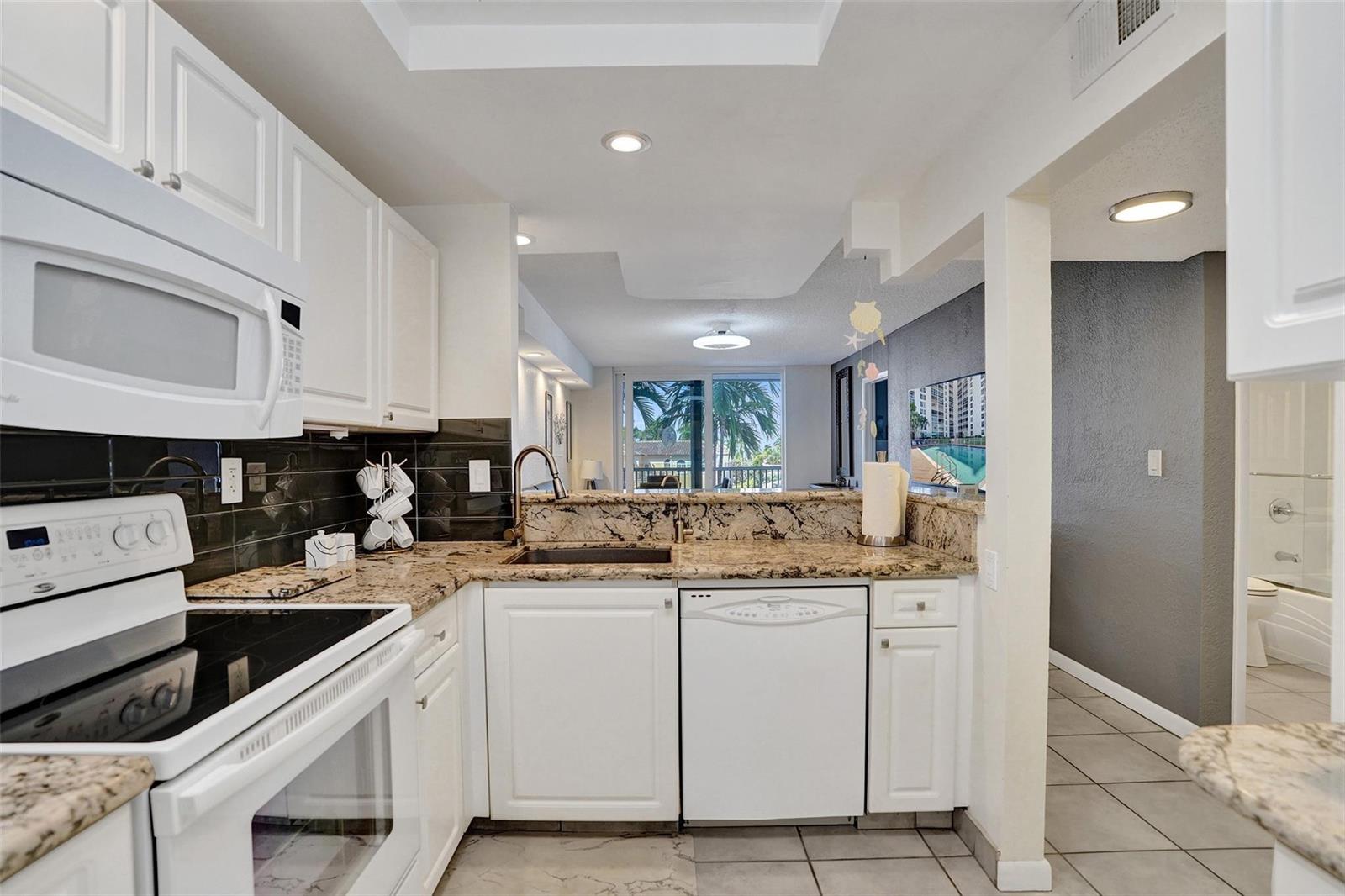 A kitchen with white cabinets, granite countertops, and a view into the living area — 1391 S Ocean Boulevard # 309, Pompano Beach FL 33062, POMPANO BEACH, FL