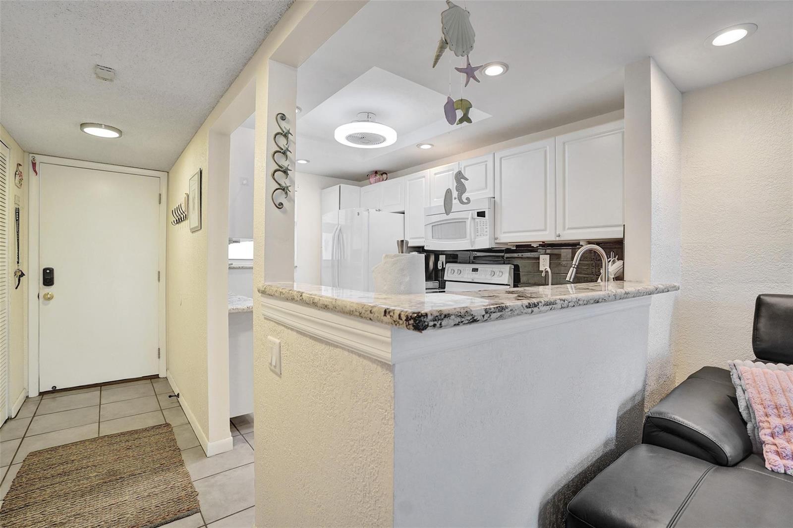 A kitchen with white cabinets and granite countertops overlooks a living area with a sofa — 1391 S Ocean Boulevard # 309, Pompano Beach FL 33062, POMPANO BEACH, FL