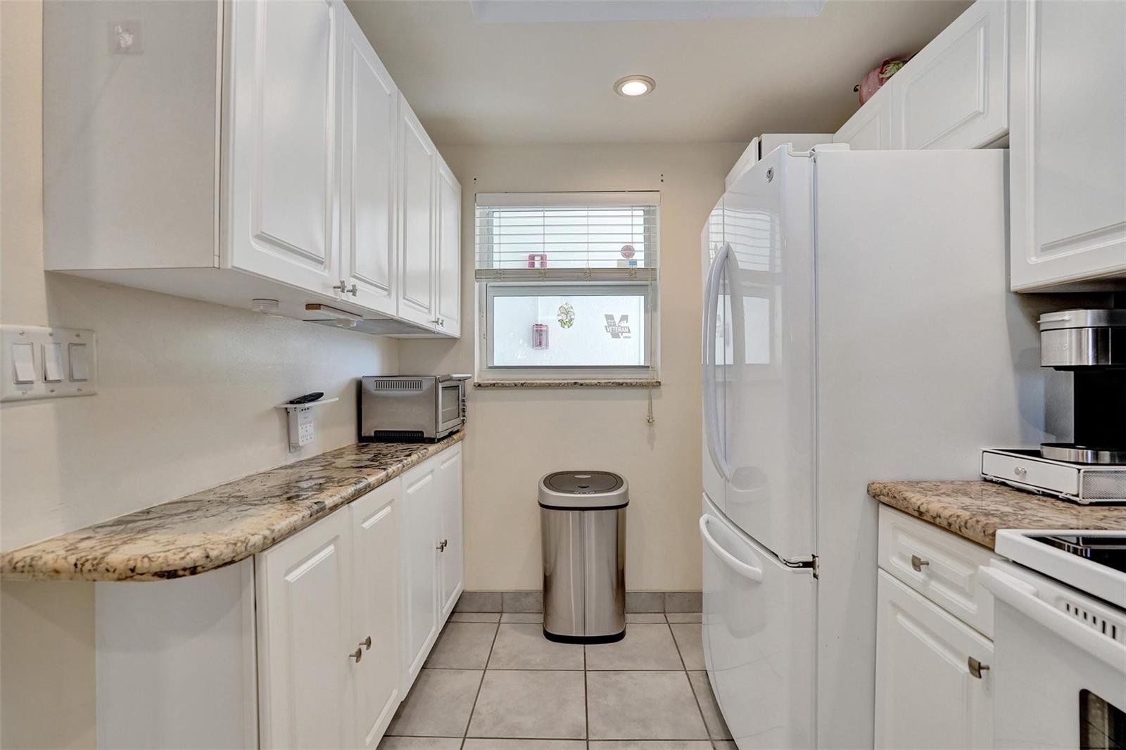 A galley kitchen features white cabinets, granite countertops, a stainless steel trash can, and appliances — 1391 S Ocean Boulevard # 309, Pompano Beach FL 33062, POMPANO BEACH, FL