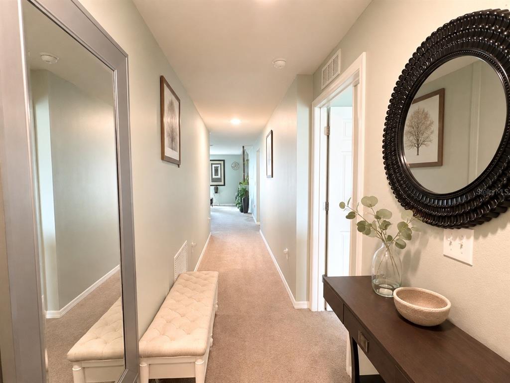 A long carpeted hallway features a console table, two mirrors, and a tufted bench — 41 WILLOW LANE, POINCIANA, FL