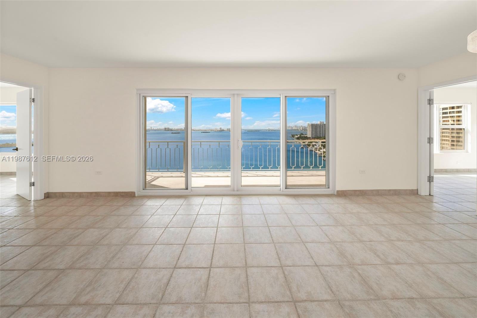 An empty room with light tile flooring features large sliding glass doors overlooking the ocean — 11111 Biscayne Blvd # 19D, Miami FL 33181, MIAMI, FL