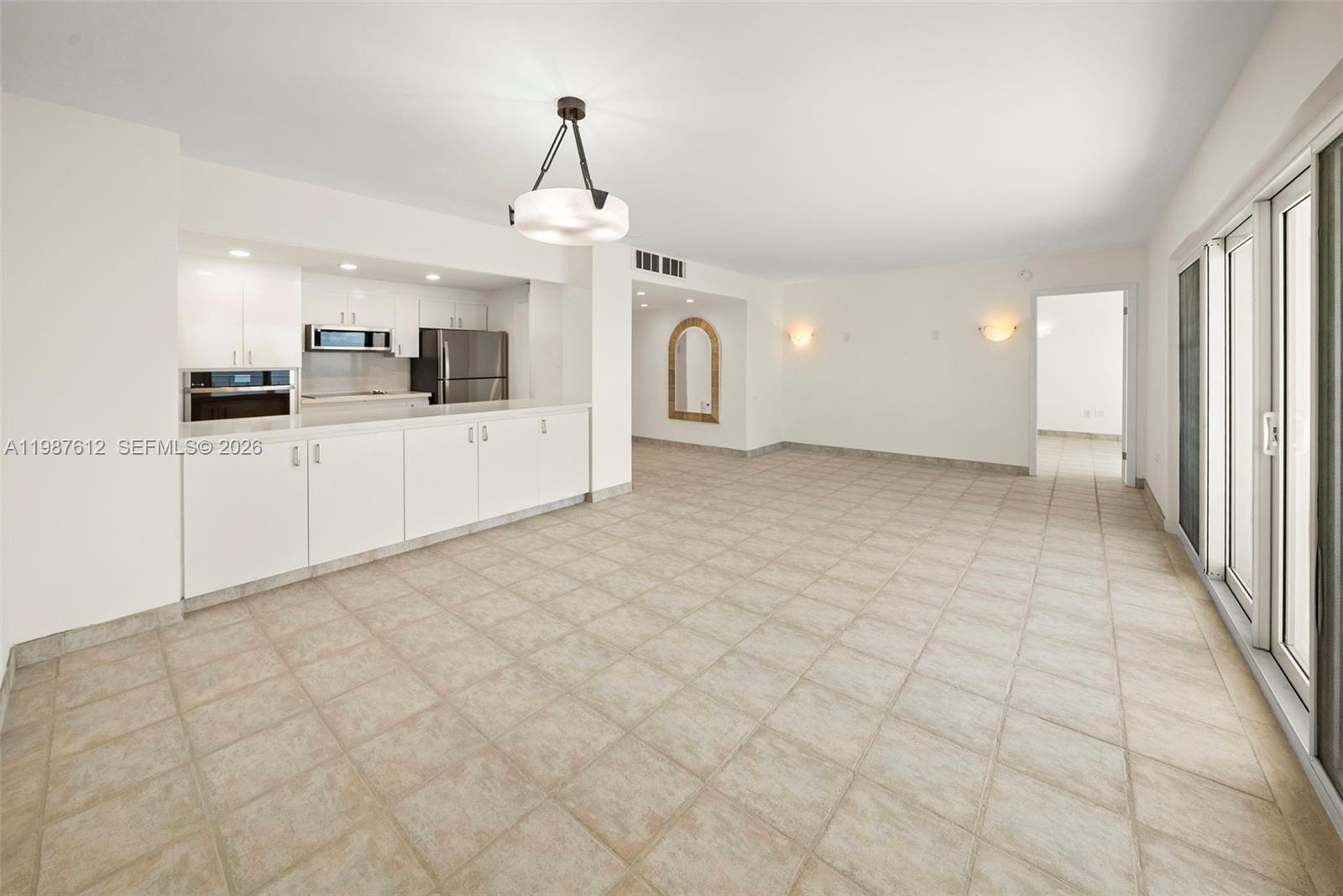 An open-concept kitchen and living area features white cabinetry, tile flooring, and sliding glass doors — 11111 Biscayne Blvd # 19D, Miami FL 33181, MIAMI, FL