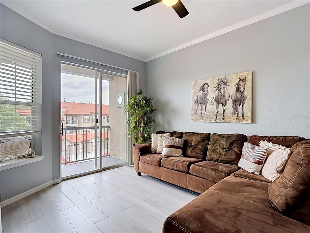 A living room features a brown sectional sofa, horse wall art, and a sliding glass door — 18107 PEREGRINES PERCH PLACE UNIT 6304, LUTZ, FL