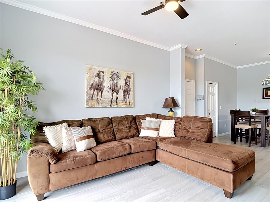 A living room features a brown sectional sofa, a horse painting, and a dining area — 18107 PEREGRINES PERCH PLACE UNIT 6304, LUTZ, FL