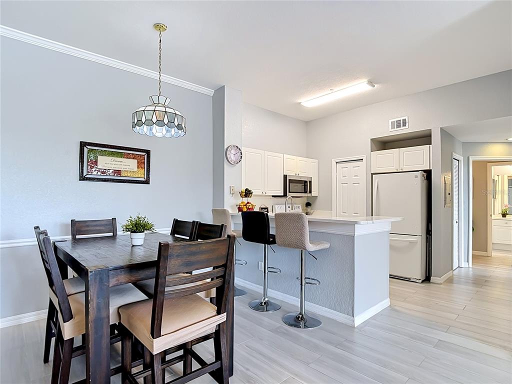 A dining area with a wooden table sits adjacent to a kitchen with bar seating — 18107 PEREGRINES PERCH PLACE UNIT 6304, LUTZ, FL