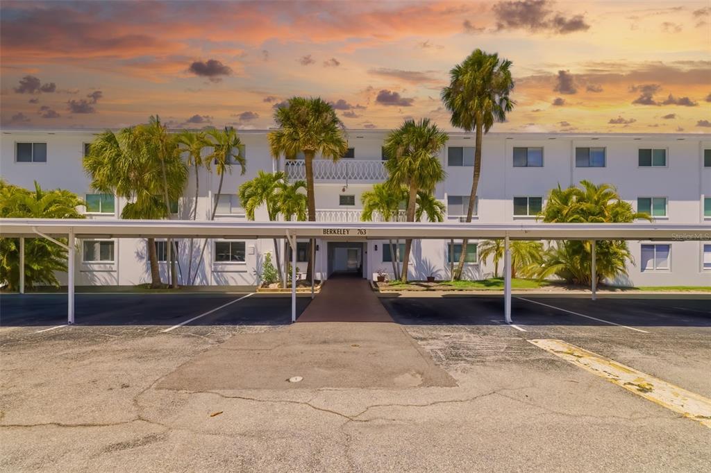 The exterior of a white multi-story apartment building features a covered parking area and palm trees — 763 JOHN RINGLING BOULEVARD UNIT 22, SARASOTA, FL