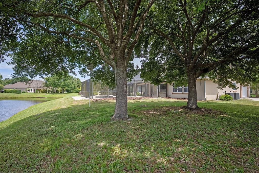 A grassy backyard features two large oak trees, a screened-in pool, and a nearby pond — 265 MOSES CREEK BOULEVARD, ST AUGUSTINE, FL