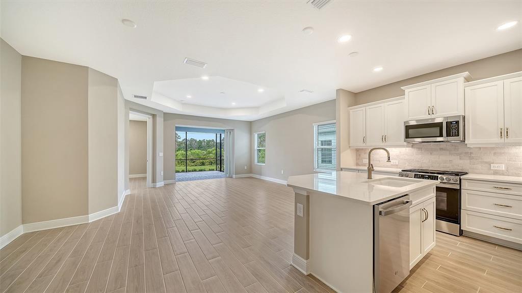 A kitchen with white cabinets and an island opens into a living area with tile floors — 2373 BLUE MAHOE LANE, SARASOTA, FL