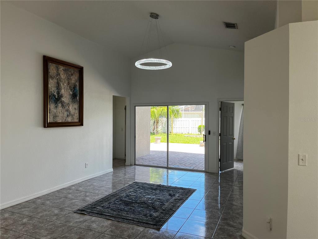 A living room with tile floors, a modern chandelier, and sliding glass doors to a patio — 5007 TERRA VISTA WAY, ORLANDO, FL
