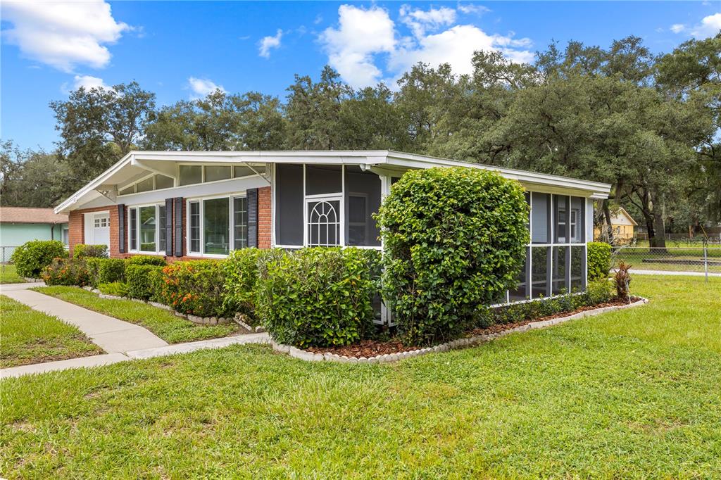 A single-story house with a brick facade, screened-in porch, and surrounding lawn under a blue sky — 3622 E LAMBRIGHT STREET, TAMPA, FL