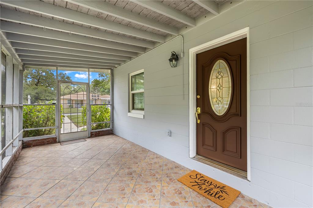 A covered porch features a brown front door, tiled flooring, and a screened-in enclosure — 3622 E LAMBRIGHT STREET, TAMPA, FL