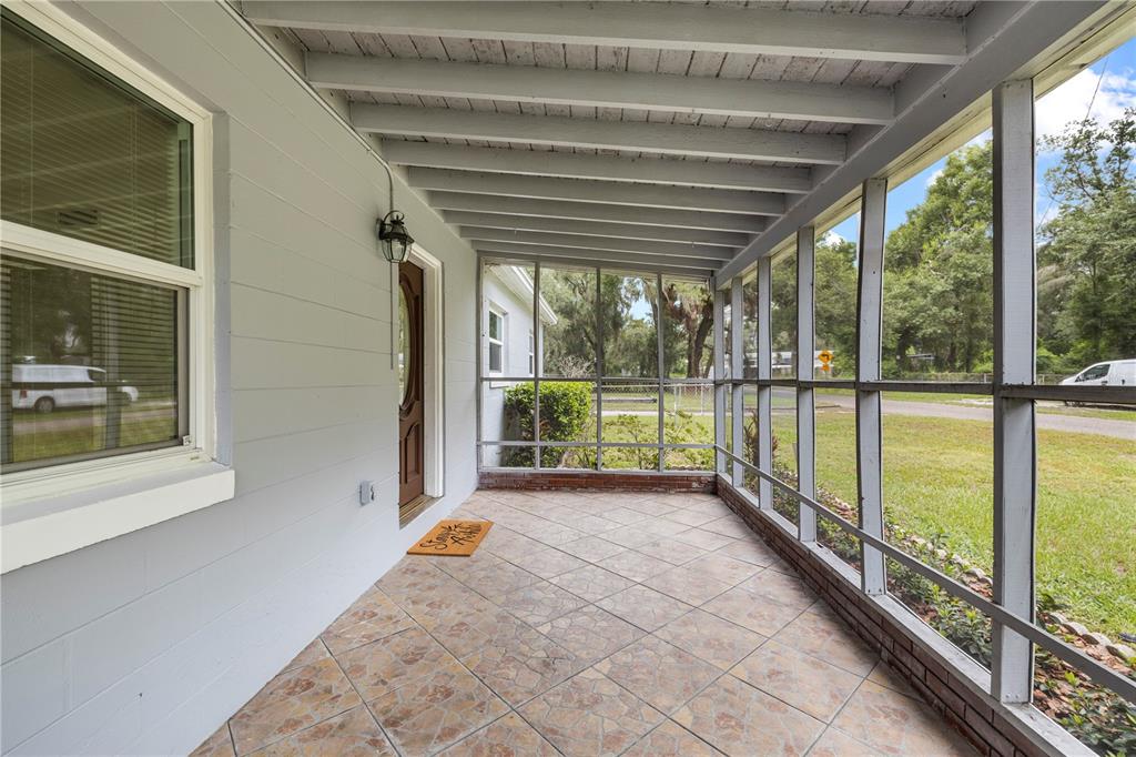 A screened-in porch with tiled flooring, a wooden door, and exposed ceiling beams — 3622 E LAMBRIGHT STREET, TAMPA, FL