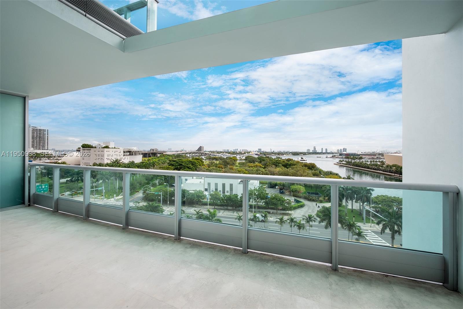 A balcony with a glass railing overlooks a park, a waterway, and a city skyline — 900 BISCAYNE BLVD # 909, Miami FL 33132, MIAMI, FL