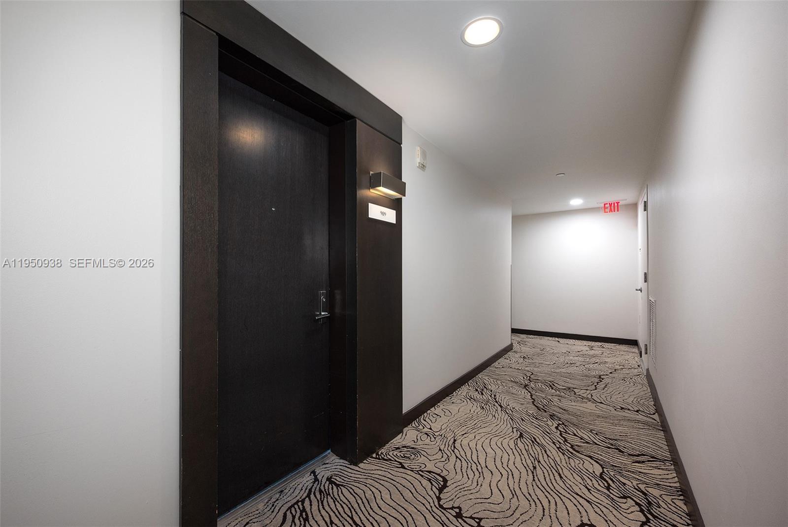 A dark wood door with a room number sign sits in a carpeted apartment hallway — 900 BISCAYNE BLVD # 909, Miami FL 33132, MIAMI, FL