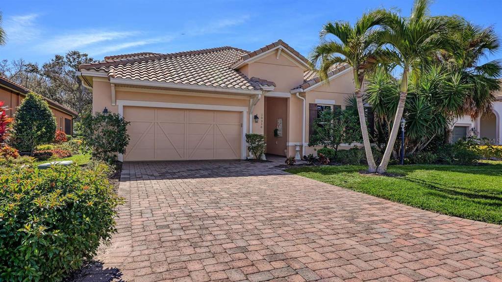 A single-story house with a tan stucco exterior, a two-car garage, and a brick driveway — 10310 EASTWOOD DRIVE, BRADENTON, FL
