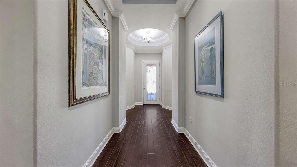 A hallway with dark wood floors leads to a white door under a domed ceiling — 10310 EASTWOOD DRIVE, BRADENTON, FL