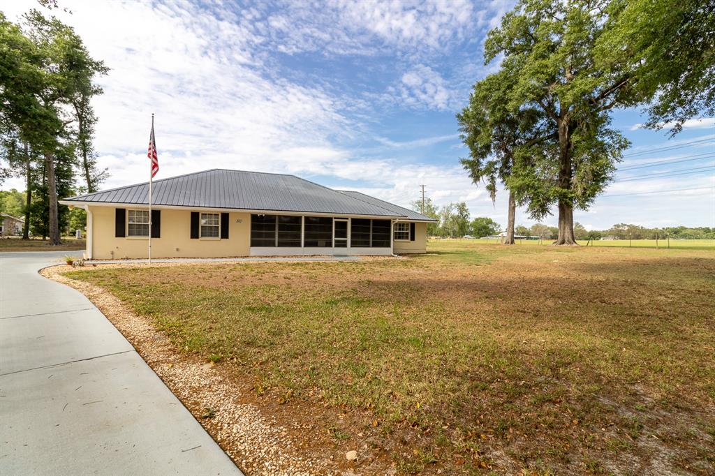 A single-story house with a metal roof, screened porch, and an American flag in front — 300 SW BRIGHTON COURT, FORT WHITE, FL