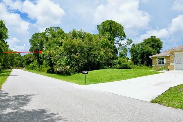 A paved road leads toward a vacant, tree-covered lot next to a residential house — 2328 REDFERN STREET, PORT CHARLOTTE, FL