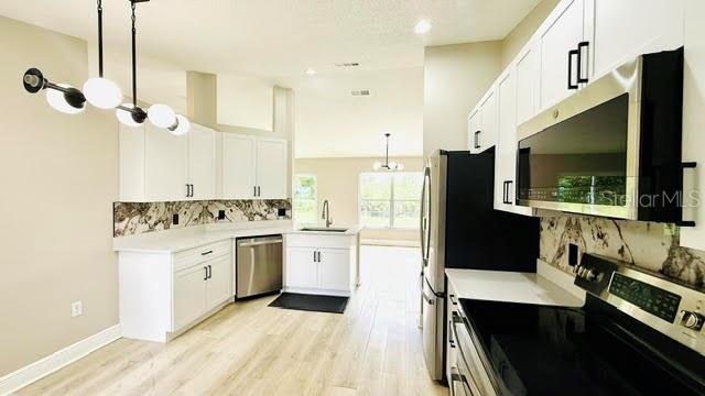 A modern kitchen features white cabinets, stainless steel appliances, and a unique stone backsplash — 15613 GREATER GROVES BOULEVARD, CLERMONT, FL