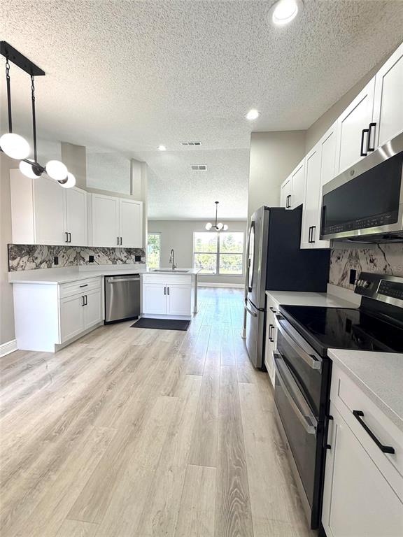A modern kitchen features white cabinets, stainless steel appliances, and light wood-look flooring — 15613 GREATER GROVES BOULEVARD, CLERMONT, FL