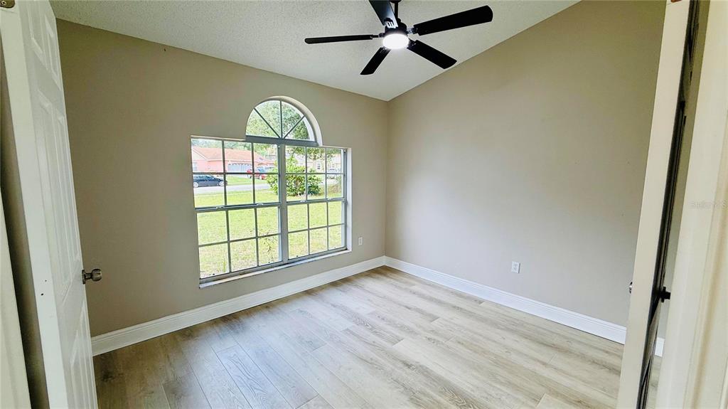 An empty room with light-colored walls, wood-look flooring, a ceiling fan, and a large window — 15613 GREATER GROVES BOULEVARD, CLERMONT, FL