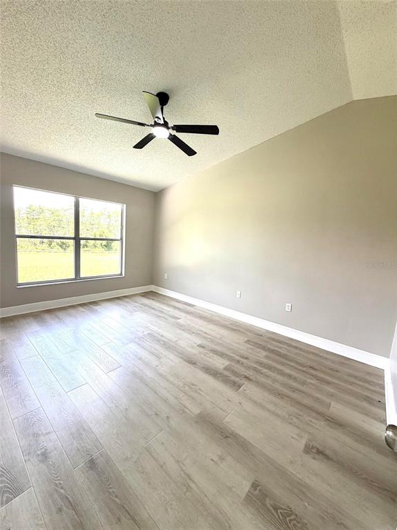 An empty room features light wood-look flooring, beige walls, a ceiling fan, and a large window — 15613 GREATER GROVES BOULEVARD, CLERMONT, FL