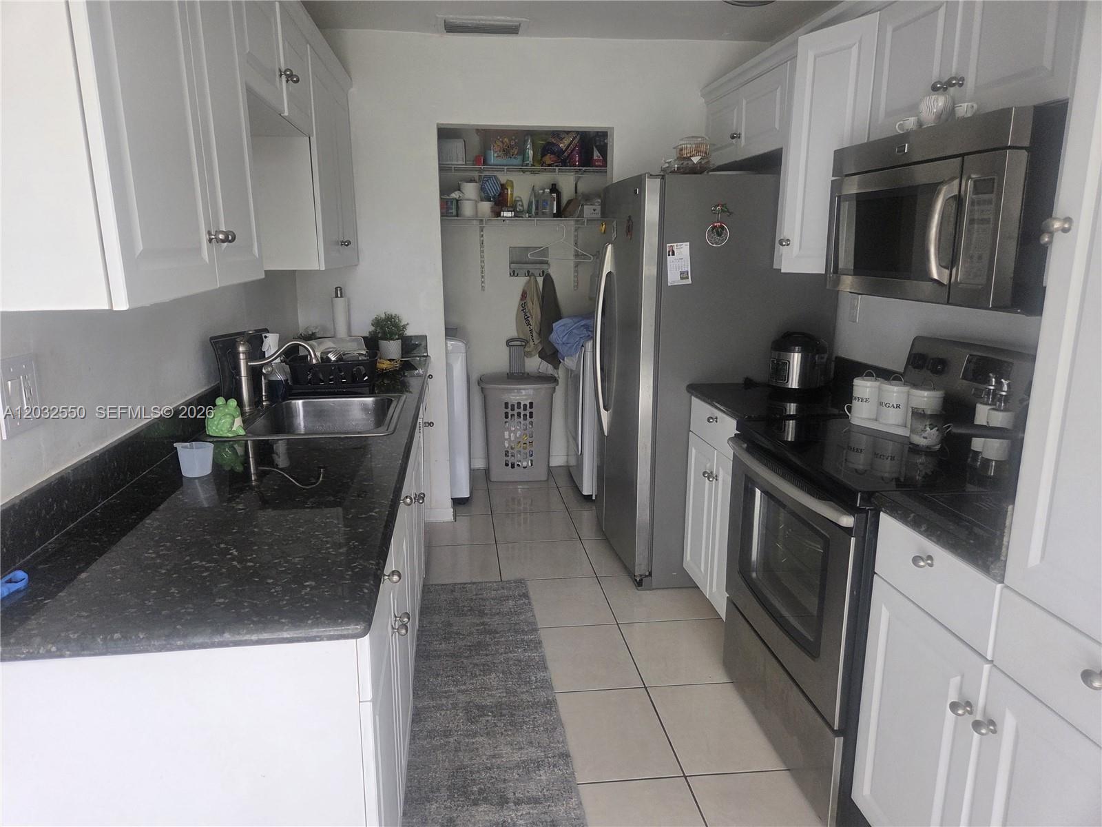 A galley kitchen features white cabinets, dark granite countertops, stainless steel appliances, and tile flooring — 11871 SW 123rd Pl, Miami FL 33186, MIAMI, FL