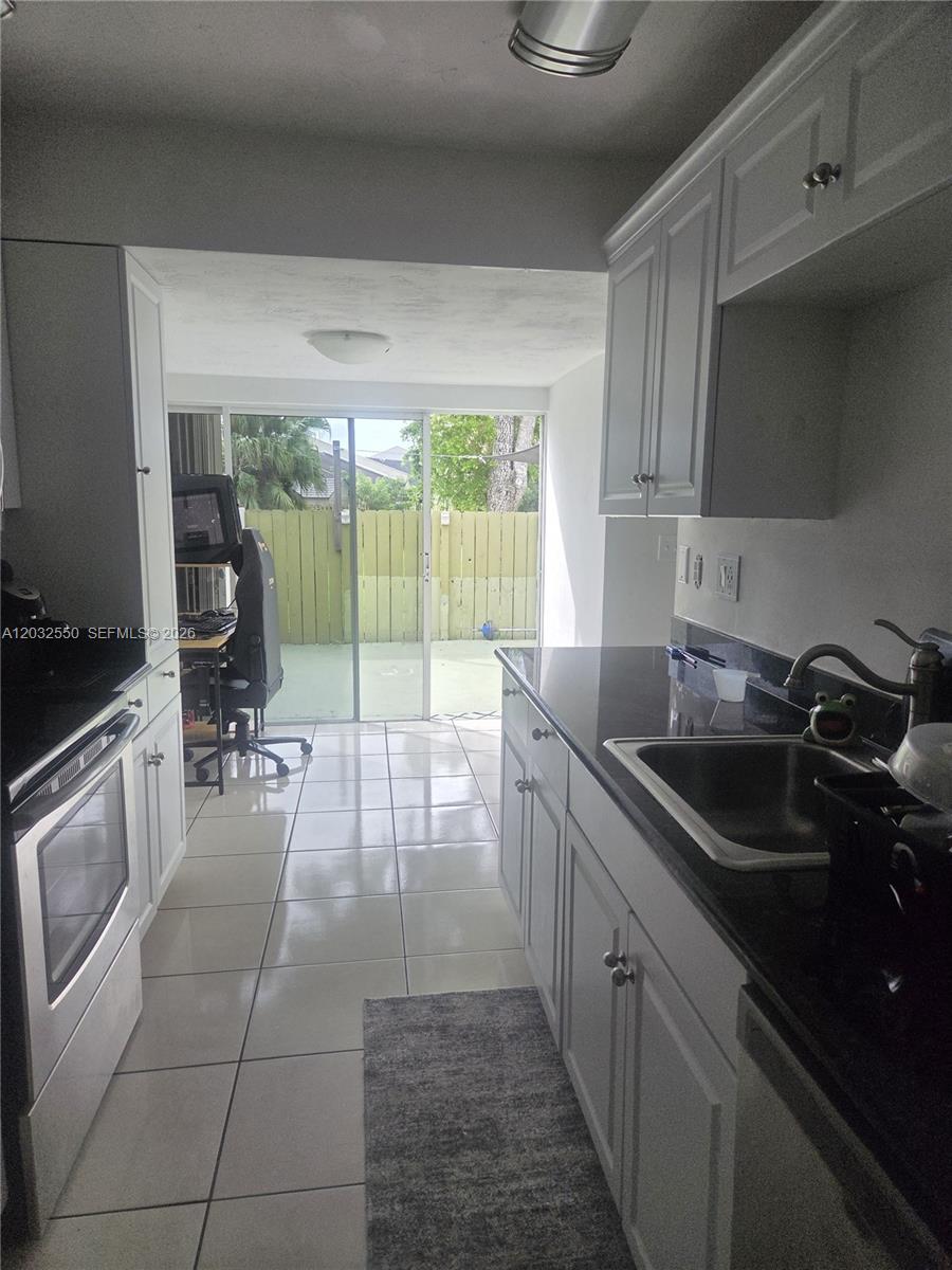 A galley kitchen features white cabinets, dark countertops, and a sliding glass door to a patio — 11871 SW 123rd Pl, Miami FL 33186, MIAMI, FL