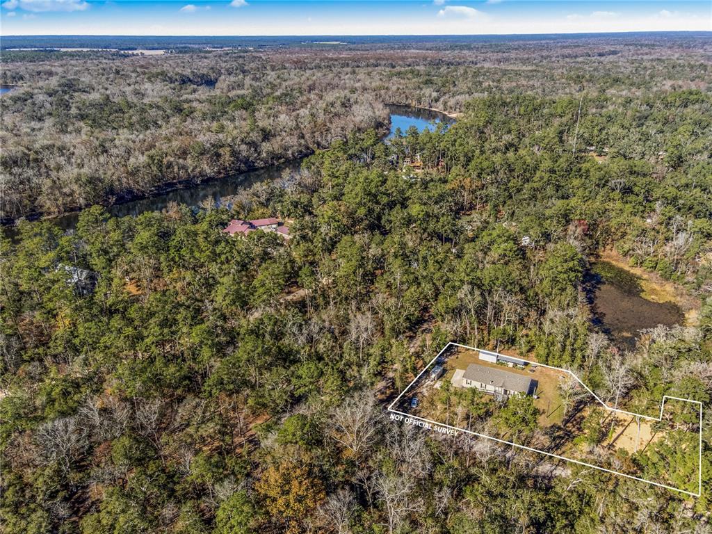 An aerial view shows a house on a wooded lot near a river and pond — 7970 SW 14TH PLACE, BELL, FL