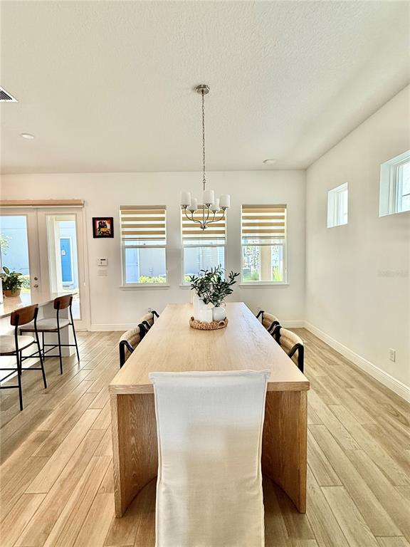 A dining room features a long wooden table, light wood-look flooring, and a central chandelier — 9922 RODBELL STREET, ORLANDO, FL