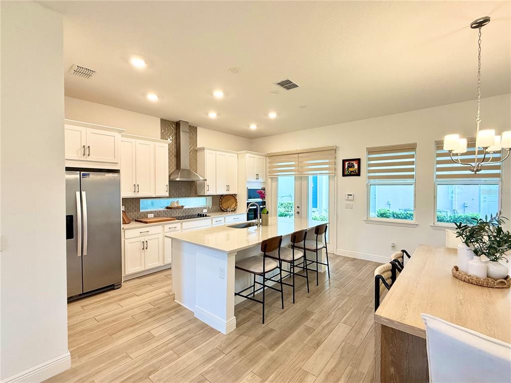 A modern kitchen features white cabinetry, a large island with bar seating, and stainless appliances — 9922 RODBELL STREET, ORLANDO, FL