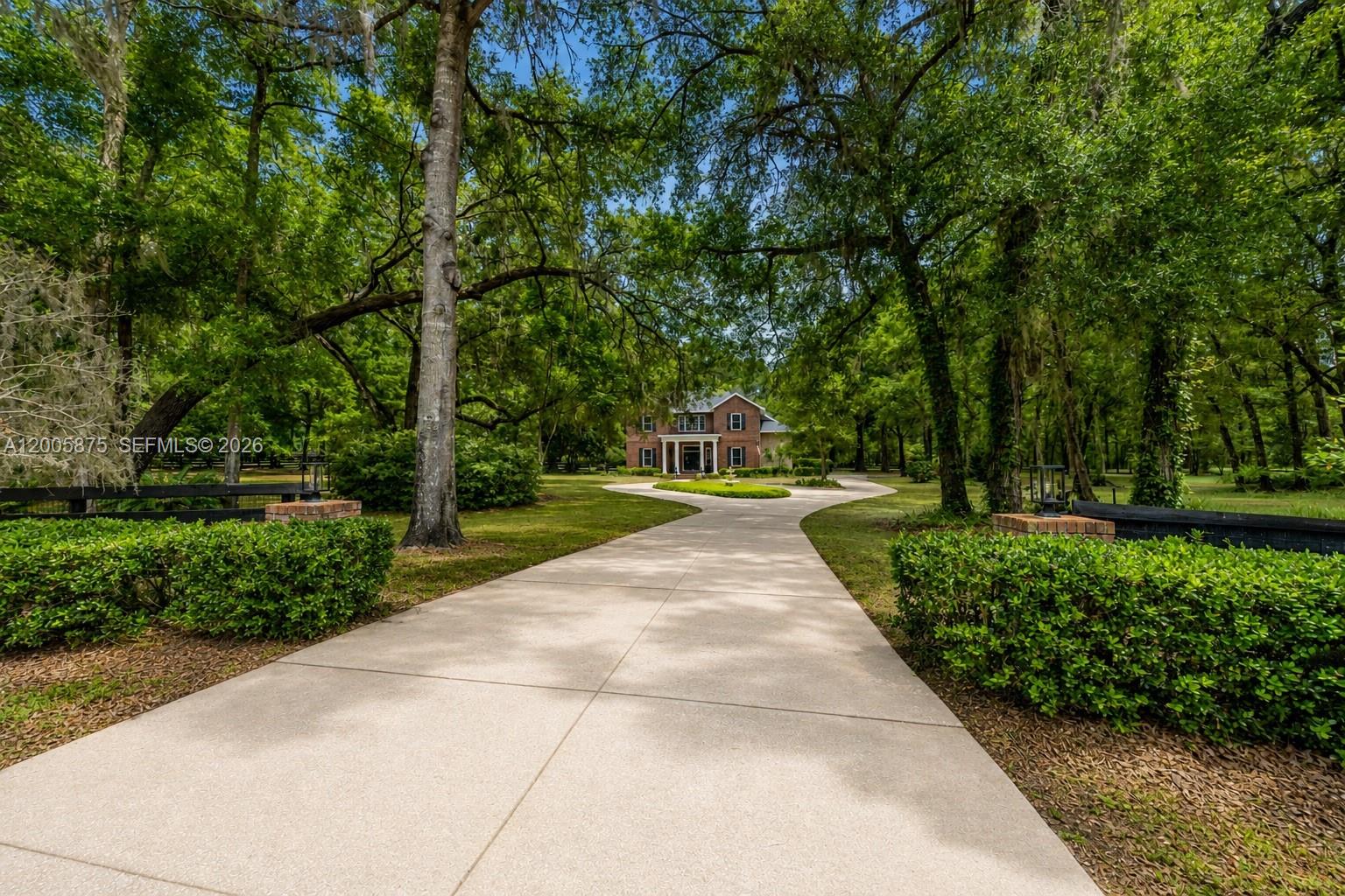 A long concrete driveway leads to a two-story brick house surrounded by mature trees — 9175 SE 7th Avenue Rd, Ocala FL 34480, OCALA, FL