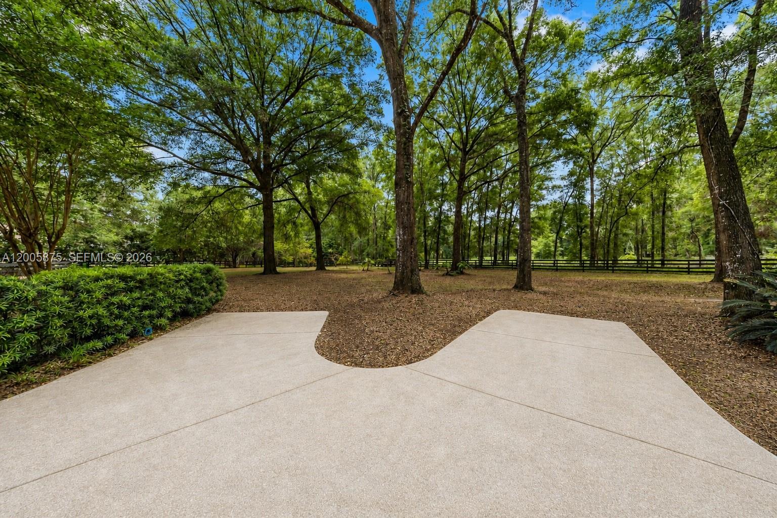 A concrete patio overlooks a wooded backyard with a fence and mature trees — 9175 SE 7th Avenue Rd, Ocala FL 34480, OCALA, FL