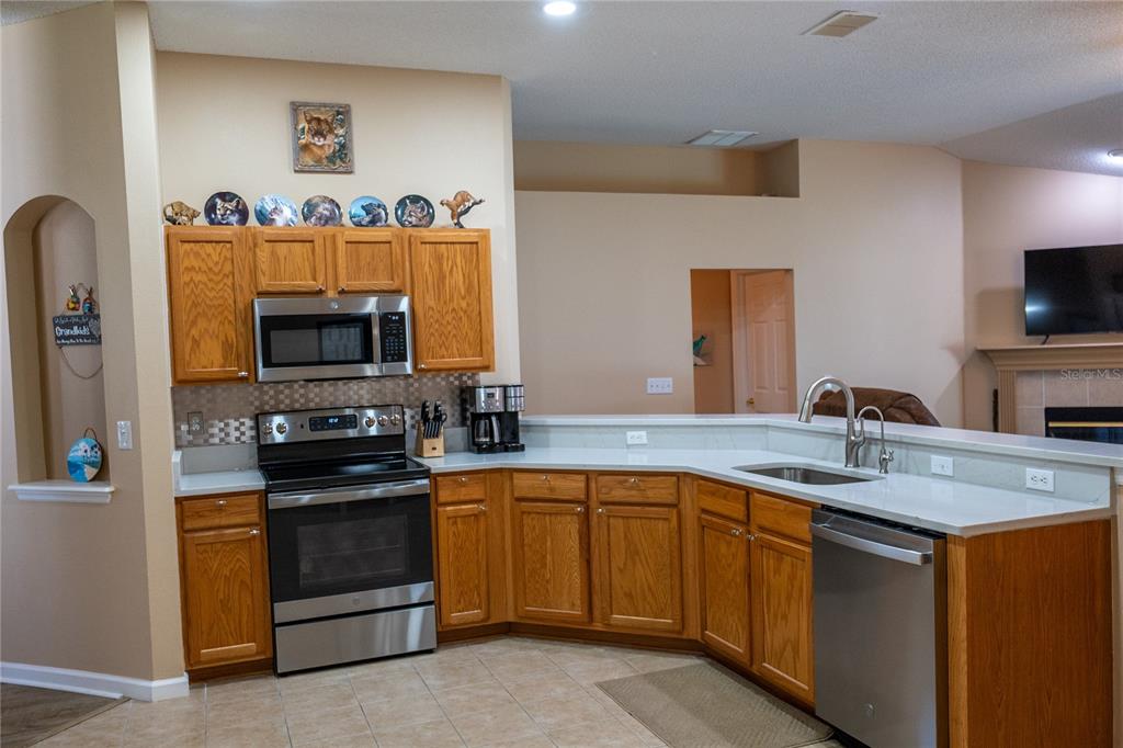 A kitchen features oak cabinets, stainless steel appliances, and a peninsula overlooking a living area — 6 BRADLEY PLACE, PALM COAST, FL