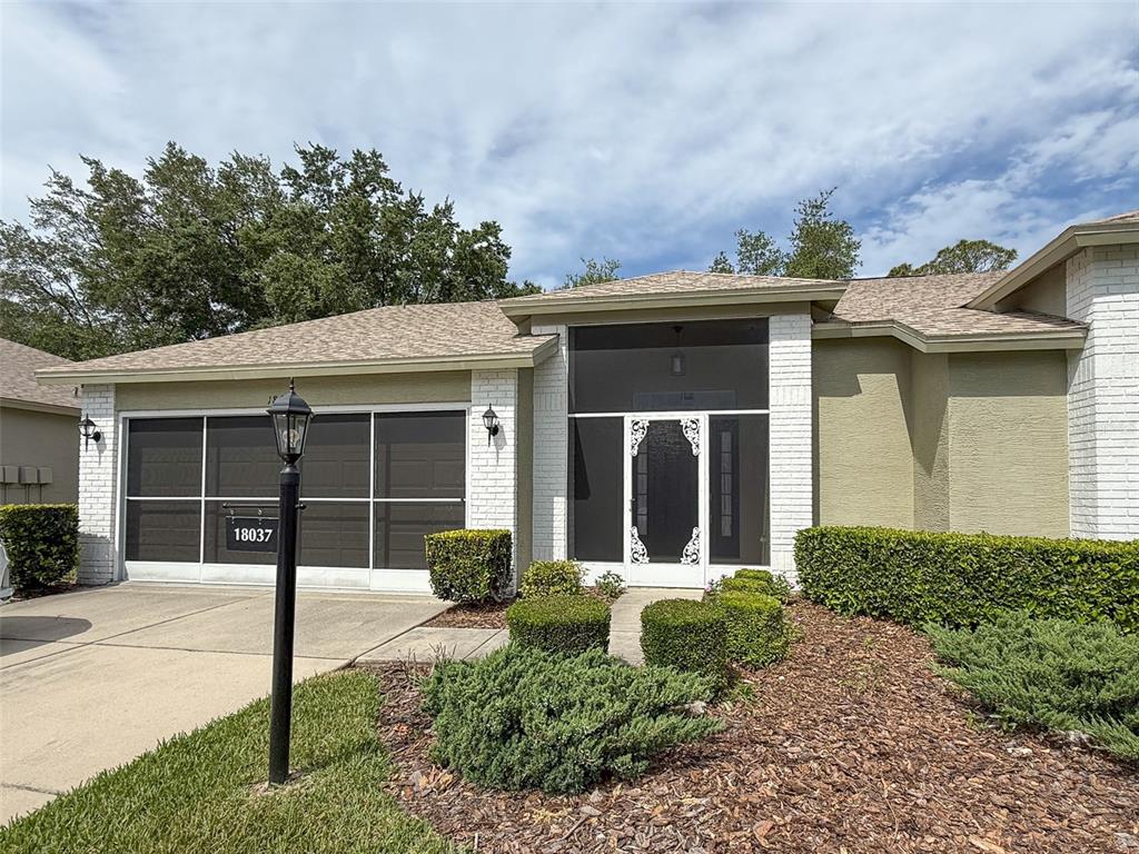 The exterior of a single-story house features a screened garage, a screened entryway, and landscaping — 18037 BAYWOOD FOREST DRIVE, HUDSON, FL