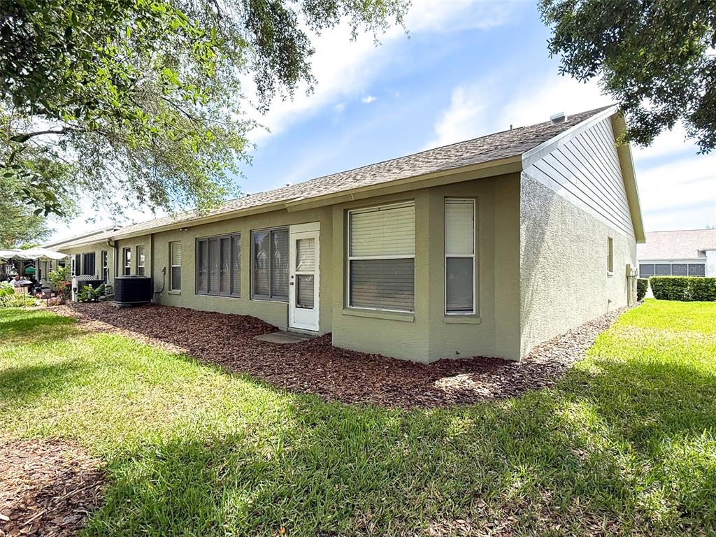 The exterior of a single-story home features tan stucco walls, a shingled roof, and landscaping — 18037 BAYWOOD FOREST DRIVE, HUDSON, FL